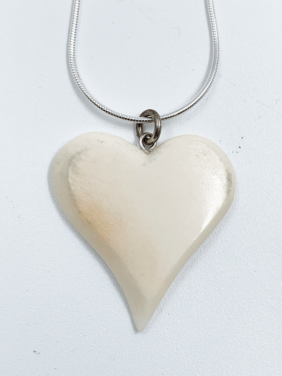 A necklace with a white heart-shaped caribou bone pendant hanging on a silver snake chain.