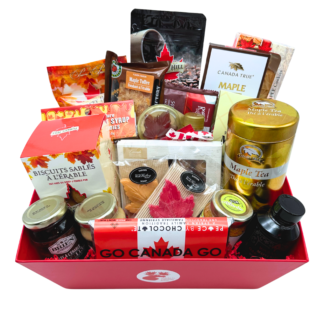 A red basket with a small circular Made in Gifts logo text and moose sticker in the center. Products inside are three spreads, a candle, soap, tea, coffee, two types of maple syrup, maple sugar, a lollipop, sea salt, maple shortbread, fudge, a chocolate bar, truffles, maple candies, toffee, and jelly.