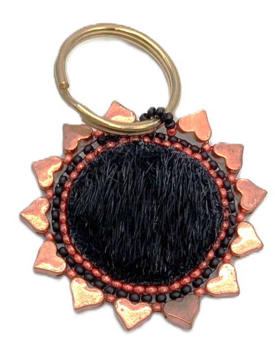 Circle keychain made of black fur and rose gold hearts surrounding it. Black and burnt orange beadwork in between.