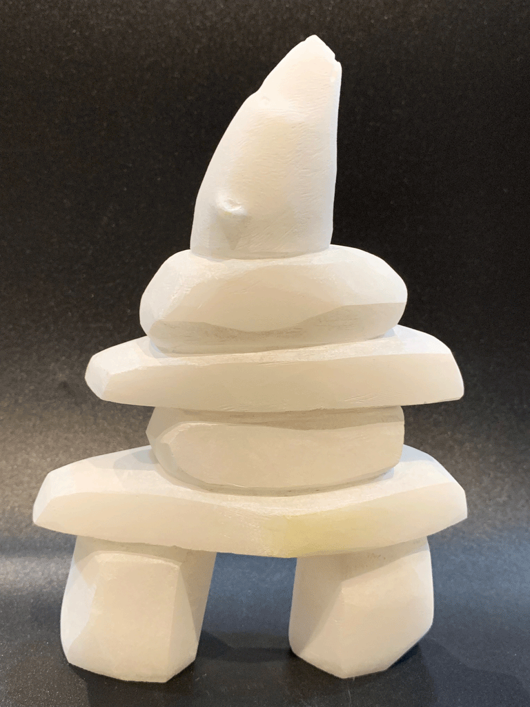 An inukshuk, the top stone of which is a polar bear head looking up, carved in one piece from white alabaster. The piece faces right in this image. The artist has used a special technique to etch fur texture into the bear and carving marks into the stone of the inukshuk for added realism.
