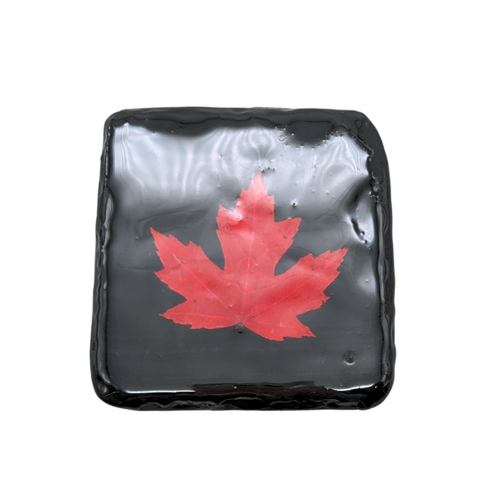 Black stone square coaster. There is a Red maple leaf in the middle of the coaster, and there is a shiny coat around it.