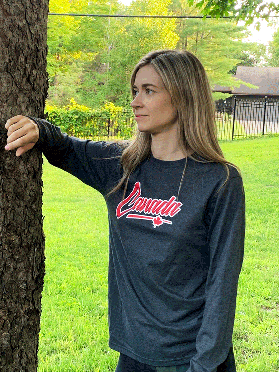 A grey long sleeve shirt. In the middle is written in red writing and a white outline "Canada". Underneath is a red and white outline underline with a maple leaf near the end.