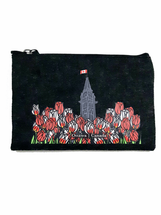 A charcoal felt pouch that features an art print of the peace tower and a field of tulips. The peace tower is in the center of the picture and is flying the Canadian flag. The dense field of flowers has red tulips and Canada 150 tulips, which are white with fiery streaks of red. At the bottom of the picture is the artists mark—a small picture of a bee. The zipper is black with a dark grey zipper puller with a rectangular piece of charcoal felt attached.