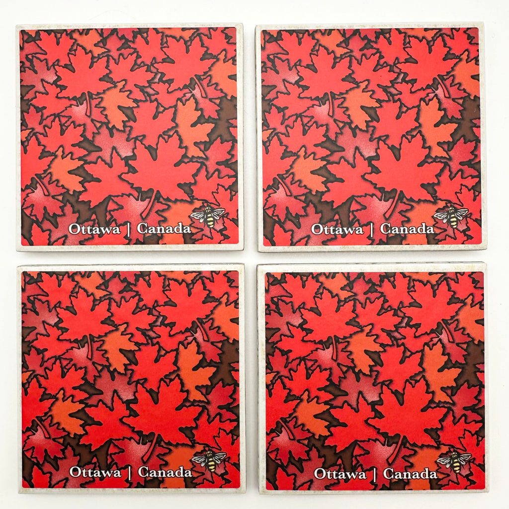 This set of four ceramic coasters features an art print of maples leaves in several shades of red. The leaves are layered on top of each other and fill the coaster from corner to corner. At the bottom of the coaster the words “Ottawa Canada” are written in white text. At the bottom right is the artist’s mark—a small picture of a bee.