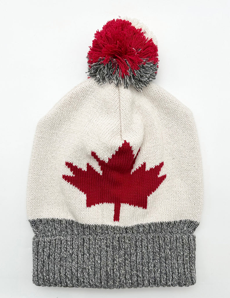 The hat is white knitted cotton with a red maple leaf on the front. The rim of the hat is grey. The hat has a large white, red and grey pom pom.