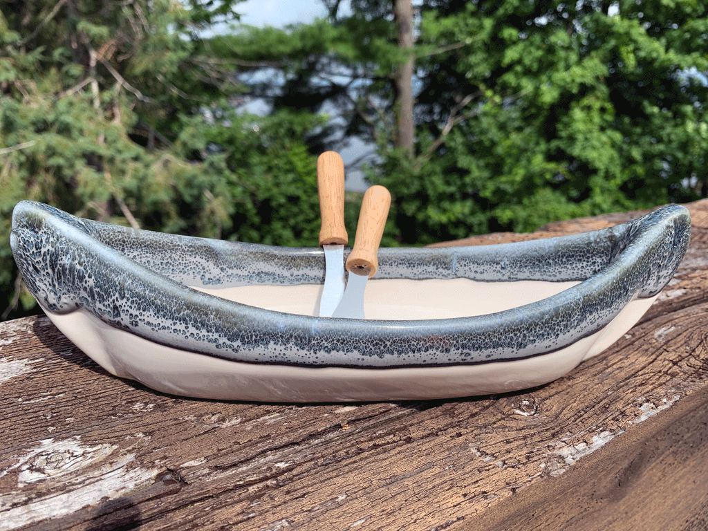 A stoneware canoe white on the bottom and a mottled grey rim. Includes two paddle spreaders.