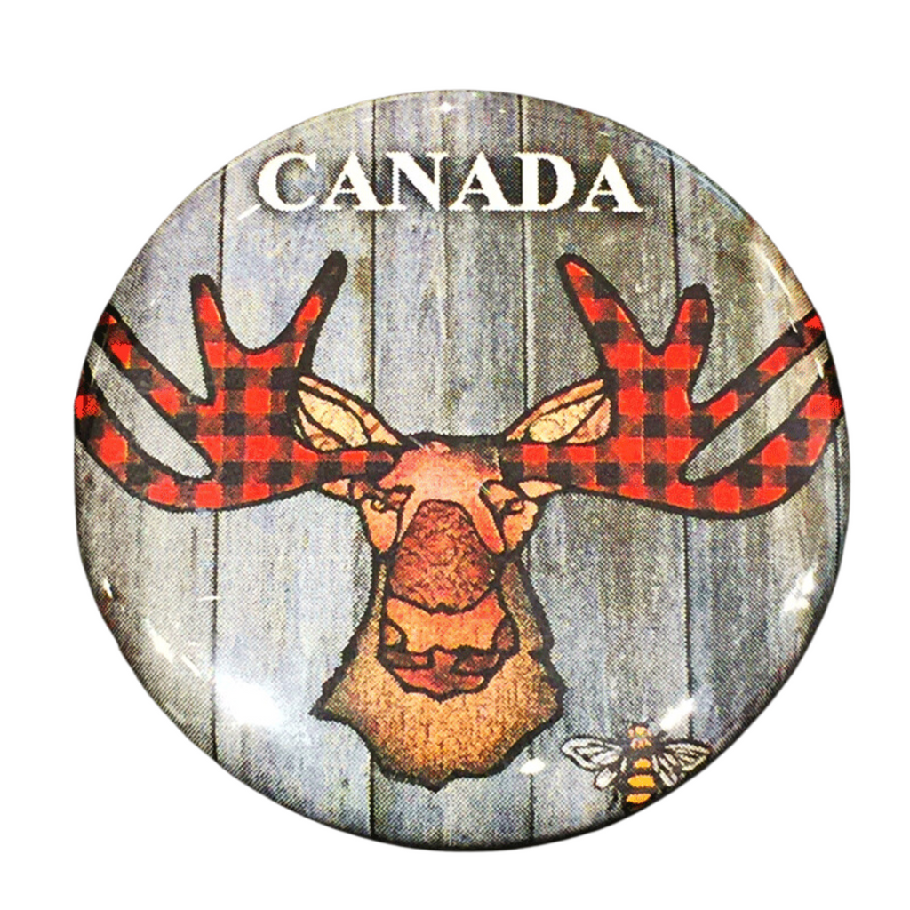 This magnet features an art print of a moose. The moose’s ear, nose, face and neck are all coloured with different shades of brown. Its antlers are coloured with red buffalo plaid. Above the moose the word Canada is written in white text. At the bottom right of the picture is the artists mark—a small picture of a bee.