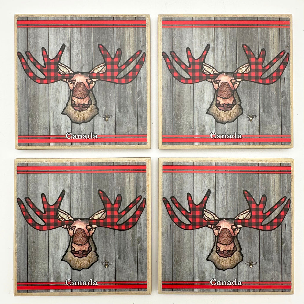 This set of four ceramic coasters features an art print of a moose. The moose’s ear, nose, face and neck are all coloured with different shades of brown. The moose’s antlers are patterned with buffalo check. Red details. Underneath the moose the word Canada has been written in white text. At the bottom right of the picture is the artists mark—a small picture of a bee.