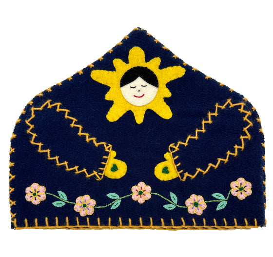 A navy tea cozy with a sun pattern around the face. Has flowers and leaves across the bottom.