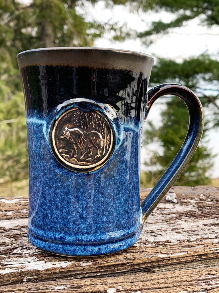 15 oz hand-thrown pottery mug with a vivid black and blue glaze and an embossed forest bear medallion in the center.