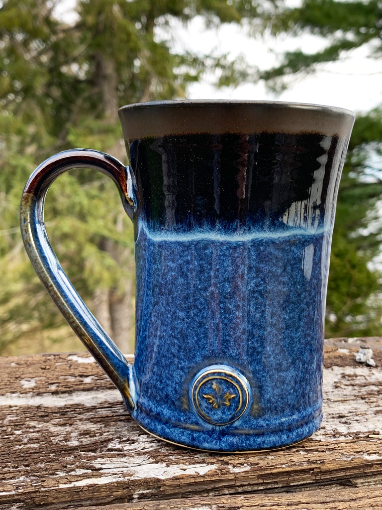 15 oz hand-thrown pottery mug with a vivid black and blue glaze and a small maple leaf embossed at the base.