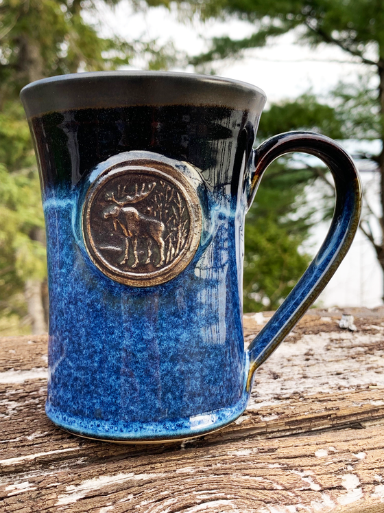 15 oz hand-thrown pottery mug with a vivid black and blue glaze and an embossed forest moose medallion in the center.