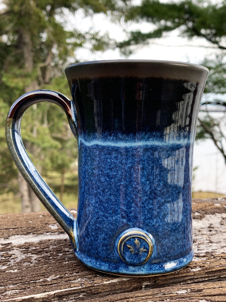 15 oz hand-thrown pottery mug with a vivid black and blue glaze and a small maple leaf embossed at the base.