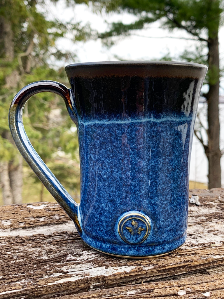 15 oz hand-thrown pottery mug with a vivid black and blue glaze and a small maple leaf embossed at the base.
