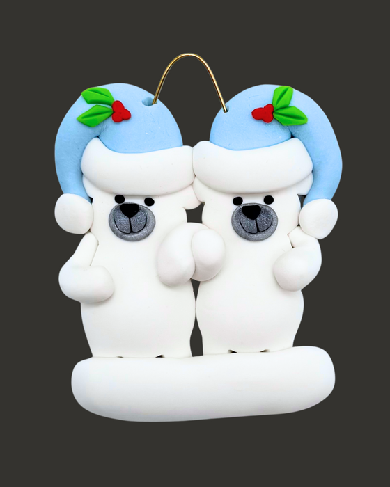 Ornament of two polar bears wearing blue hats on a black background.