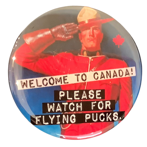 This round magnet shows a vintage picture of a saluting Canadian Mounty. Across the picture the words “welcome to canada” are printed in black text against a white stripe, and the words “please watch for flying pucks” printed in white against a black stripe. The text resembles a classic typewriter font.