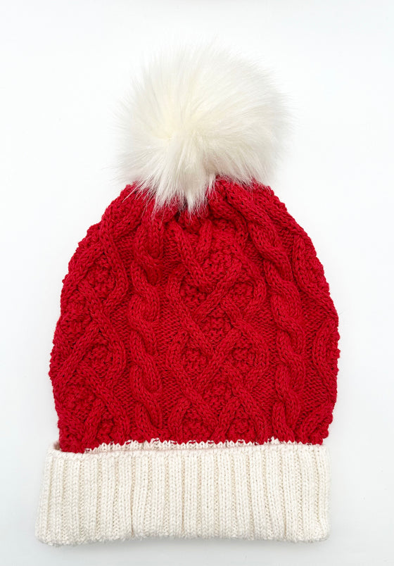 A red cable knit hat with a white bottom. Has a white pompom.