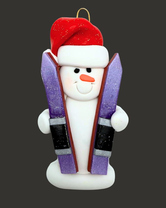 Snowman ornament with skis wearing a red hat on a black background.