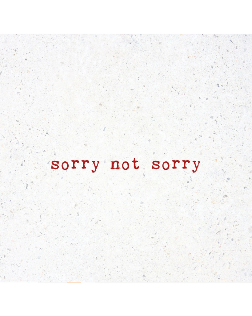 Natural white marble with "sorry not sorry" printed in red serif typeface as though by typewriter in the middle of the coaster.