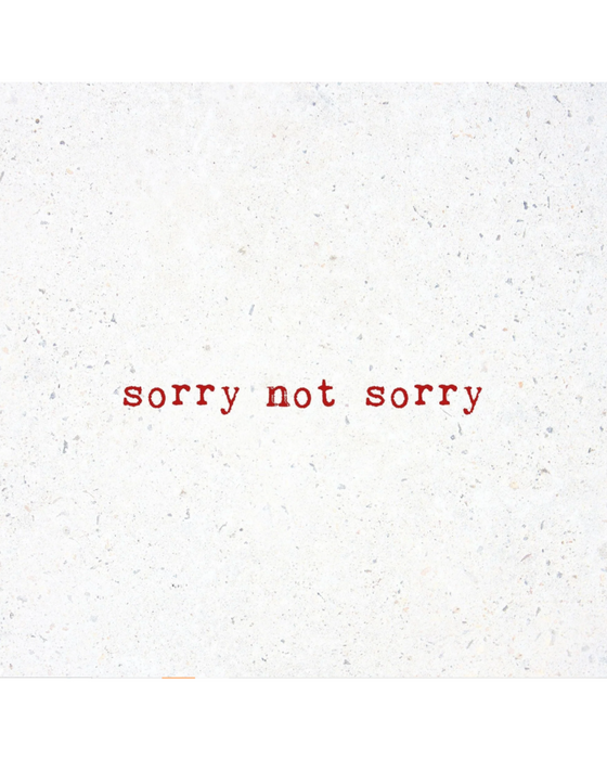 Natural white marble with "sorry not sorry" printed in red serif typeface as though by typewriter in the middle of the coaster.