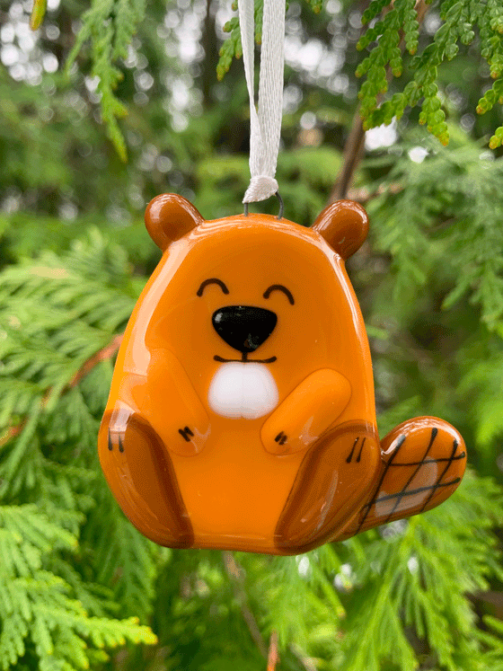 An adorably loveable beaver ornament, made of fused glass. The beaver is brown with black accents and displays a cheerful expression.