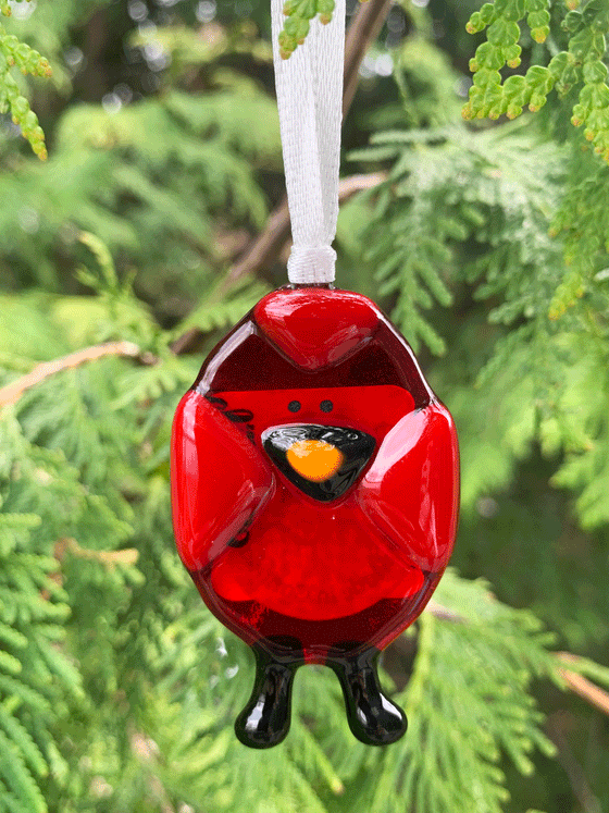 A beautiful red cardinal ornament that is made in Canada and made of fused glass. The cardinal has a black and orange beak and black feet.