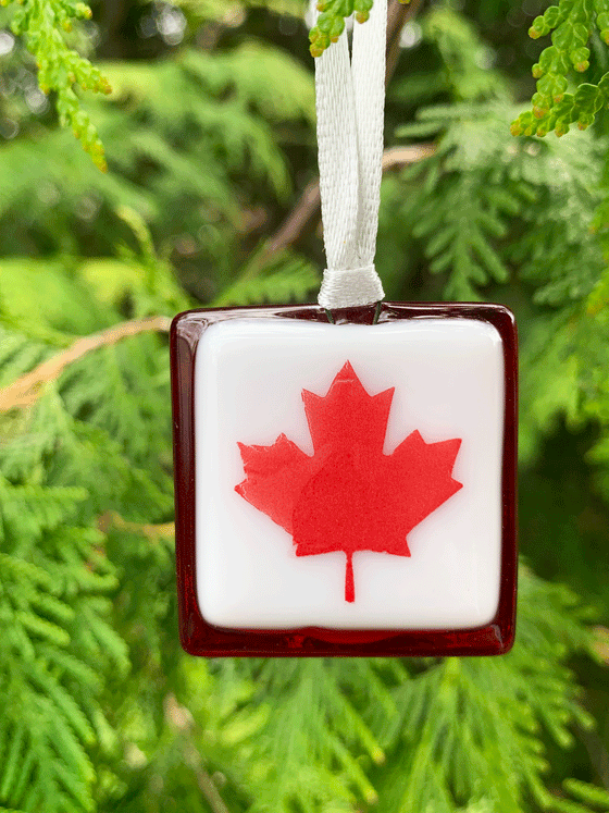 A perfectly Canadian maple leaf fused glass ornament. This piece is Canadian made and depicts a red maple leaf on a white background, framed by a darker border.