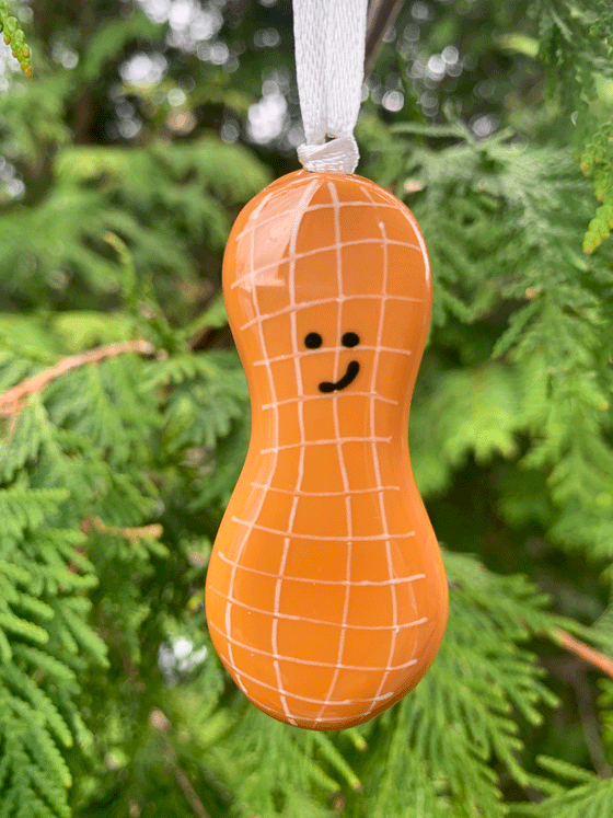A cute peanut ornament that is Canadian made from fused glass. This piece is brown with white and black accents, and the peanut is smiling.