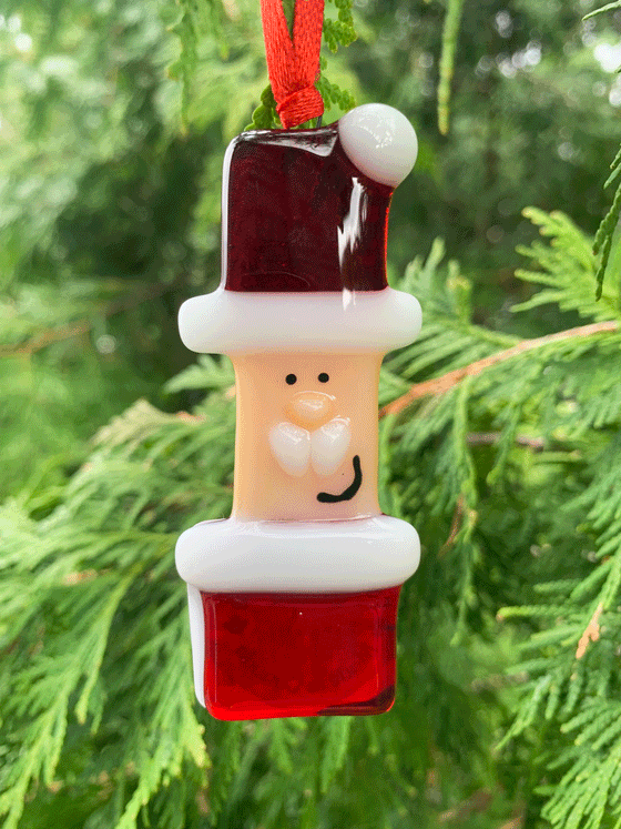 A Santa fused glass Christmas ornament that is Canadian made. Santa wears red and white and is kindly smiling.