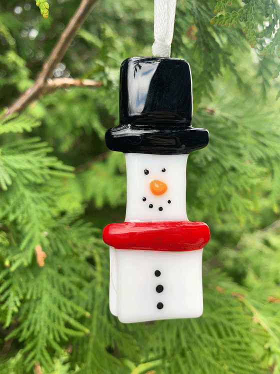 A Christmas themed snowman ornament made from fused glass. This Canadian made piece is perfect for decorating. The snowman is white and wears a black hat and red scarf.