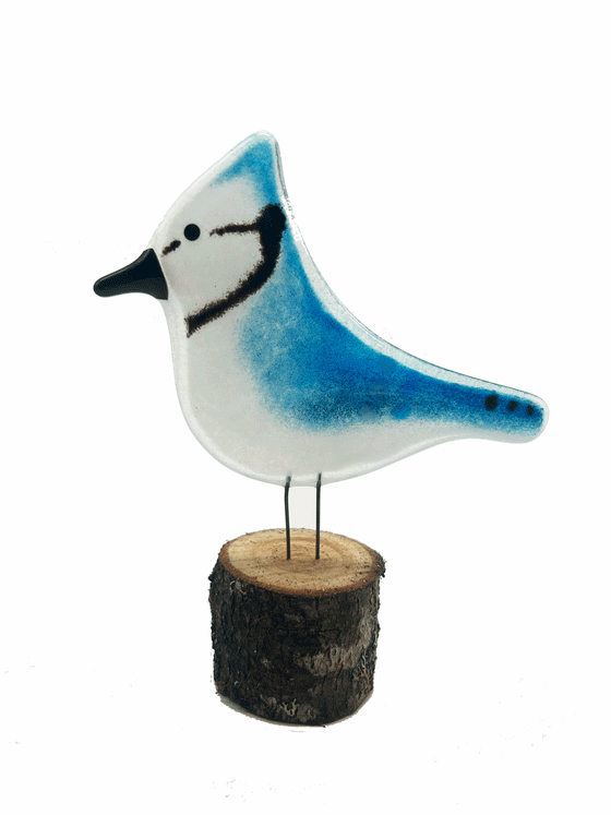 2-D glass Blue Jay. Has 2 small metal rods coming from the bottom of it that look like legs. The metal rods are attached to a piece of a tree that looks like a small tree stump. The background is white.