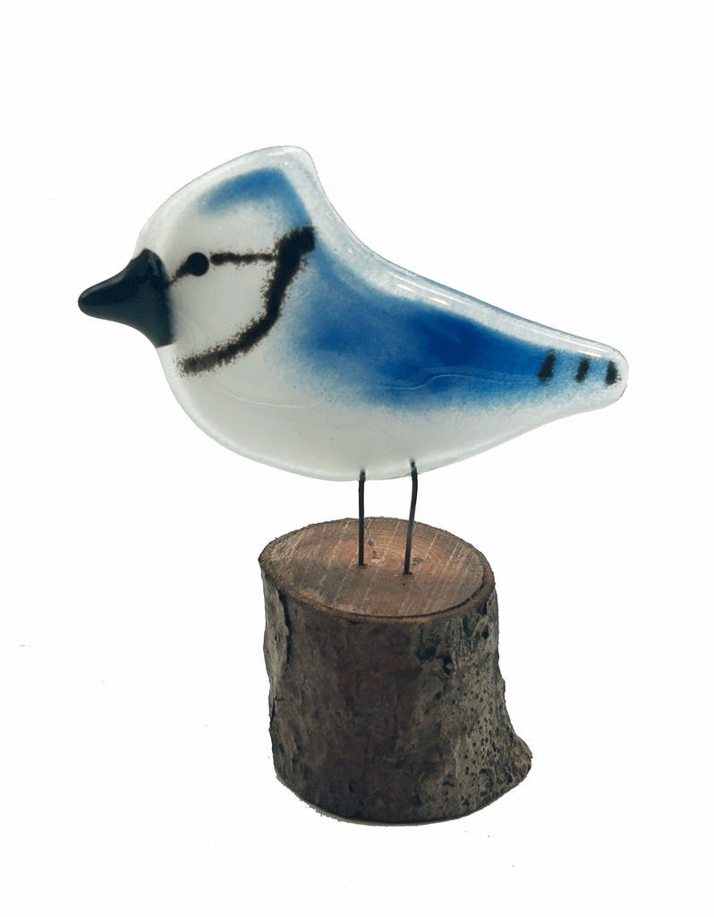 2-D Glass Blue Jay that has 2 small metal rods coming from the bottom of it that look like legs. The metal rods are attached to a piece of a tree that looks like a small tree stump. The background is white.