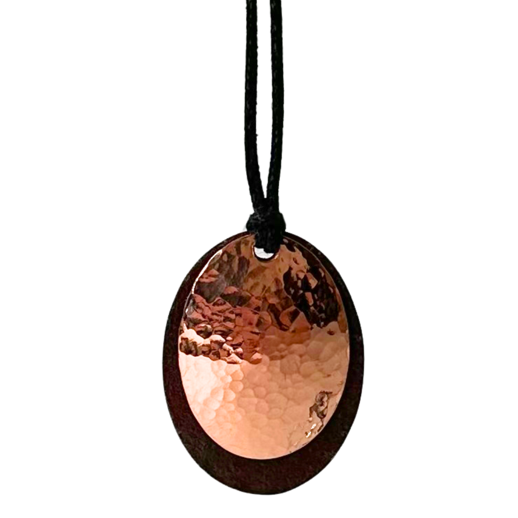A beautiful necklace made of copper and tin mounted on a leather cord. The pendant is made of two layers: antique upcycled tin cut into an oval forms the base, and then a hammered copper circle is overlaid to create stunning contrast.