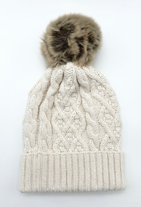 A white cable knit hat with a brown pompom.