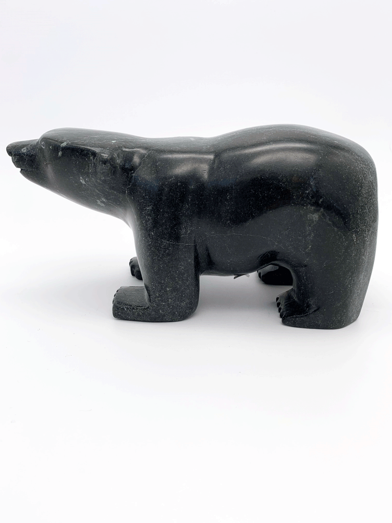 A smiling bear carved from very dark green soapstone stands on all fours, staring straight ahead. This bear faces left.
