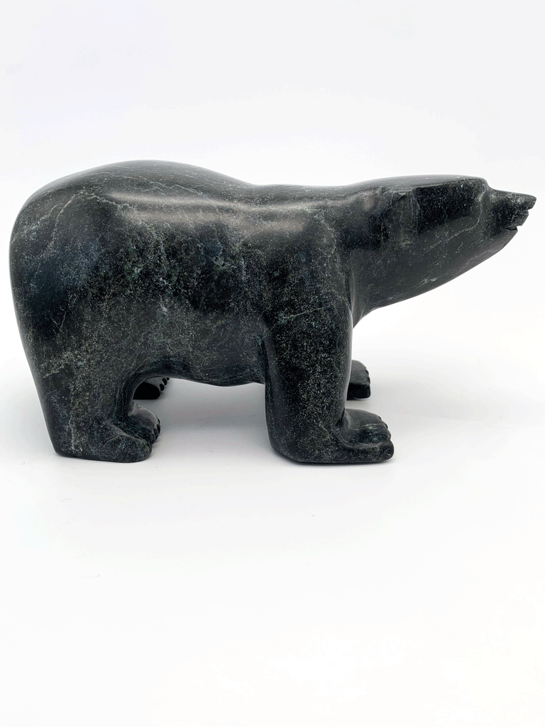 A smiling bear carved from very dark green soapstone stands on all fours, staring straight ahead. This bear faces right.