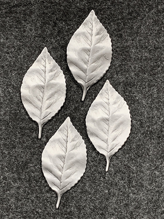 Four pewter magnets in the shape of leaves with lines tracing where the leaves' veins would be. 