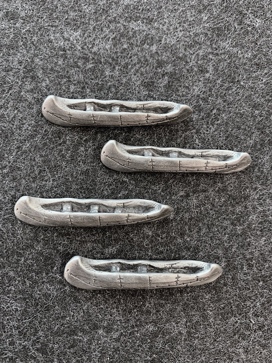 Four pewter canoes with an open top and lines along the sides from where pieces of birch bark have been stuck together. 