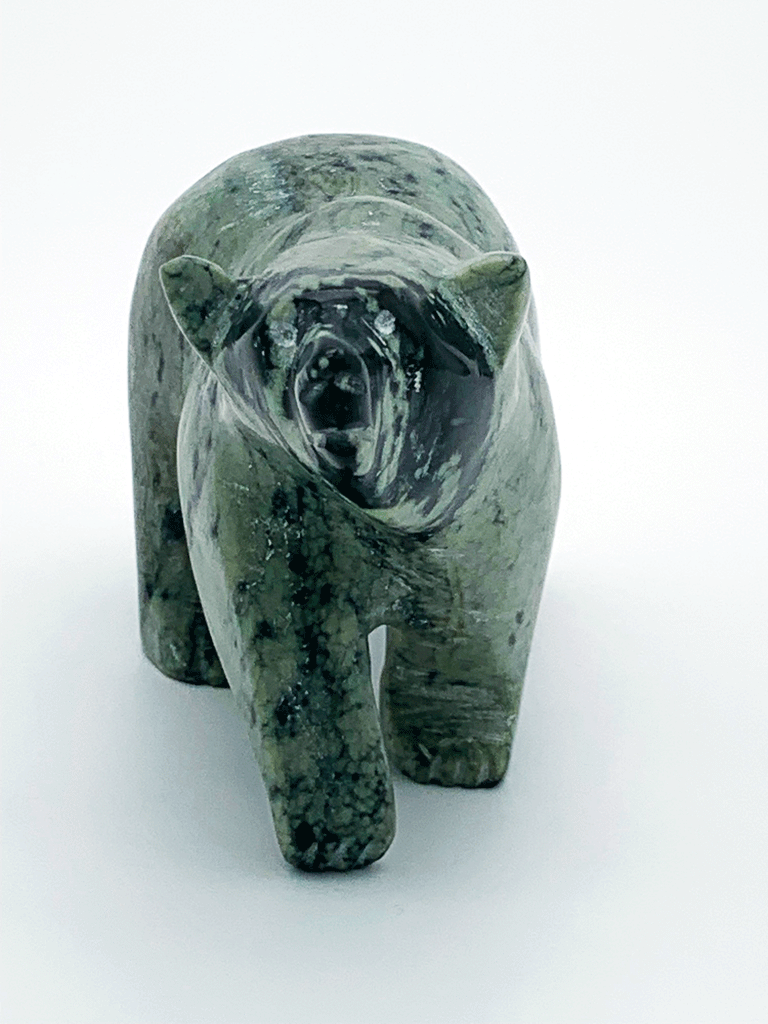 A walking bear carved from vividly contrasting green and black mottled stone. The natural mottling of the stone provides an additional layer of visual interest to the artist's smooth lines and delicate, expressive face. This bear faces the viewer.