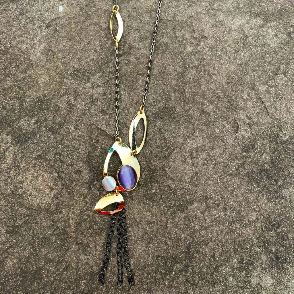 A necklace featuring  several gold leaf shapes and a purple cat's-eye glass gem. Three short brass chains hang from the bottom of the necklace
