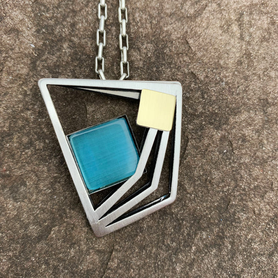 A necklace featuring an abstract silver trapezoid. The right edge of the trapezoid is drawn three times. In the center is a square of blue cat's-eye glass.