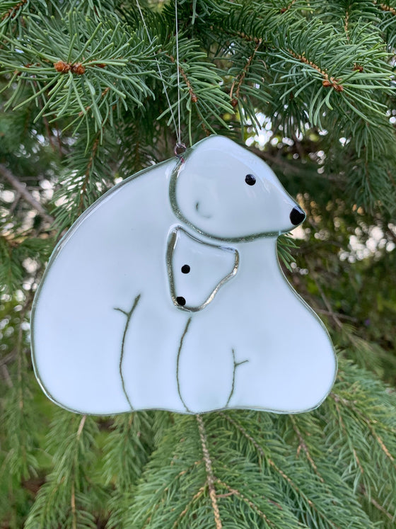 A fused glass ornament showing a mother polar bear and her cub. The cub is tucked snuggly under the mother’s chin.