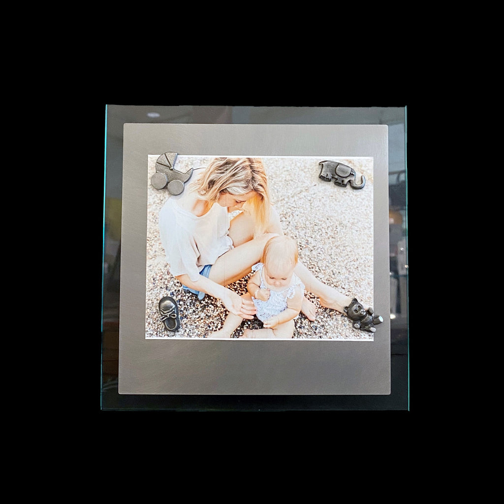 This frame consists of a square sheet of brushed steel on a larger square of glass. A photo of a woman sitting with her child is held on with the baby magnet set. 