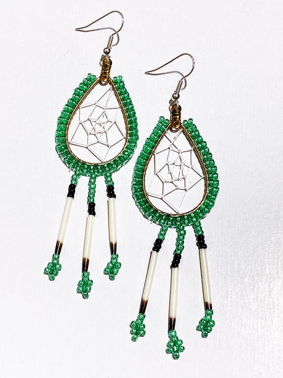 A pair of porcupine quill earrings. The hanging earrings are a tear drop shape hoop with dream catcher style weaving on the inside. Green beads are woven along the outside of the hoop and hanging off of the bottom are three strands with green and black beads, then a piece of porcupine quill, with more green beads at the end.