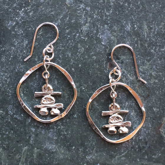 Two sterling silver Inukshuk hook earrings. Each handmade Inukshuk is unique and shaped slightly different than each other. The Inukshuk are encircled by beaten silver hoops.