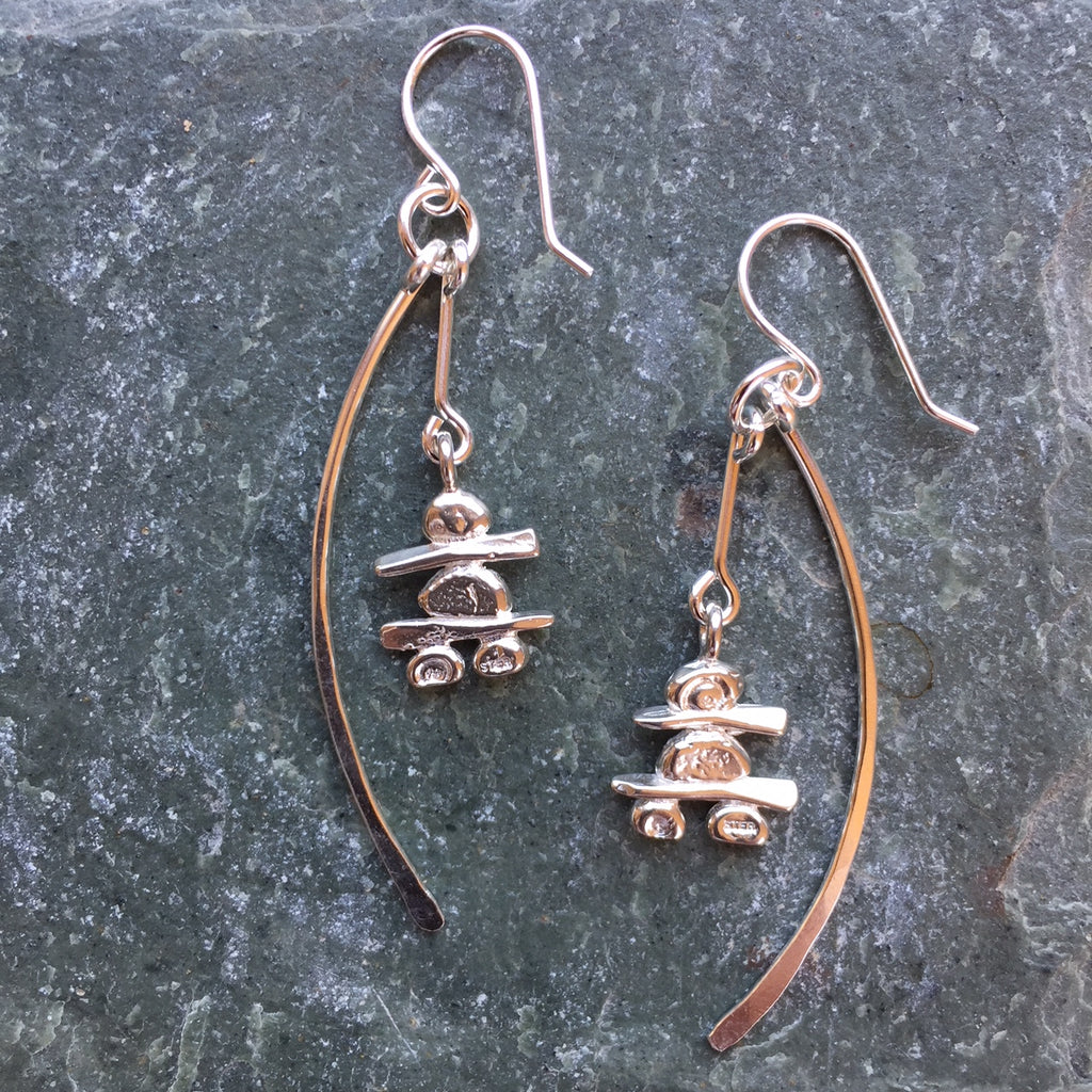 Two sterling silver hook earrings featuring an Inukshuk and a long shallow crescent. The Inukshuk hang down to the middle of the crescents. Each handmade Inukshuk is unique and shaped slightly different than each other.