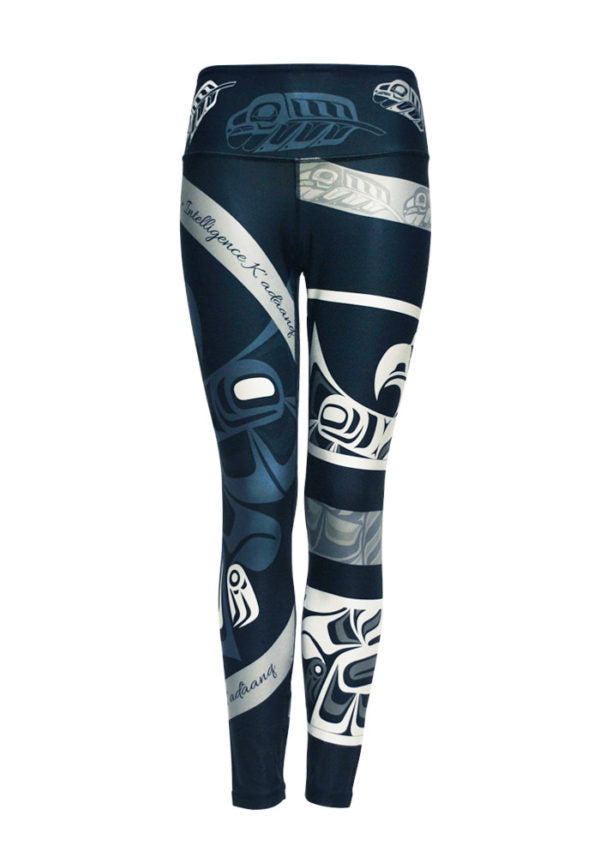 These navy blue leggings are decorated with a motif of Haida eagles and eagle feathers, drawn in lighter blue, grey and white. A ring of feathers circles the waist. A white eagle with spread wings encircles the left leg, and another raven in light blue encircles the right. Also around the right leg are two grey stripes with the word “intelligence” written in English and Haida.