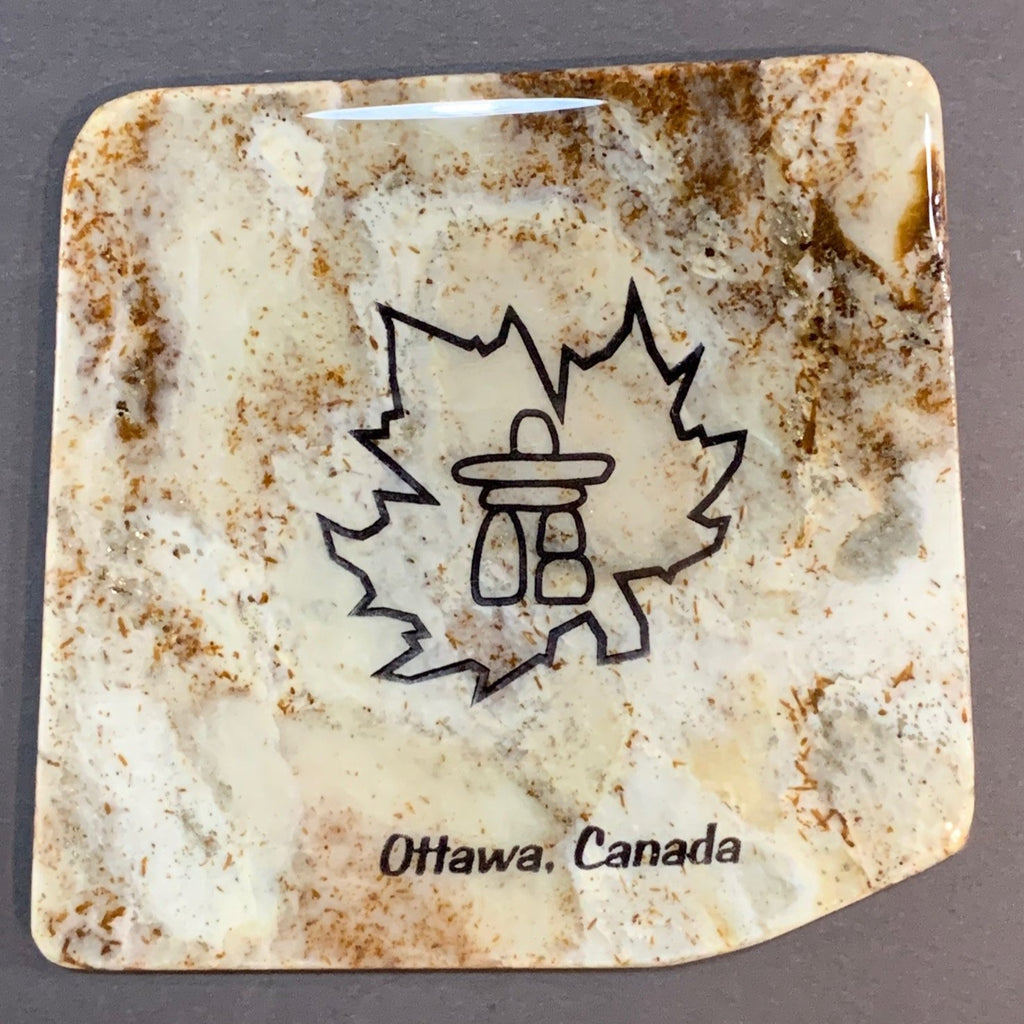 This coaster features the image of an inukshuk inside of a maple leaf, the words Ottawa, Canada below. The image is on a piece of canadian shield marble with mineral lines running through in unique colours, lines, and patterns. The coaster is finished with a clear coat, giving it a shiny finish.