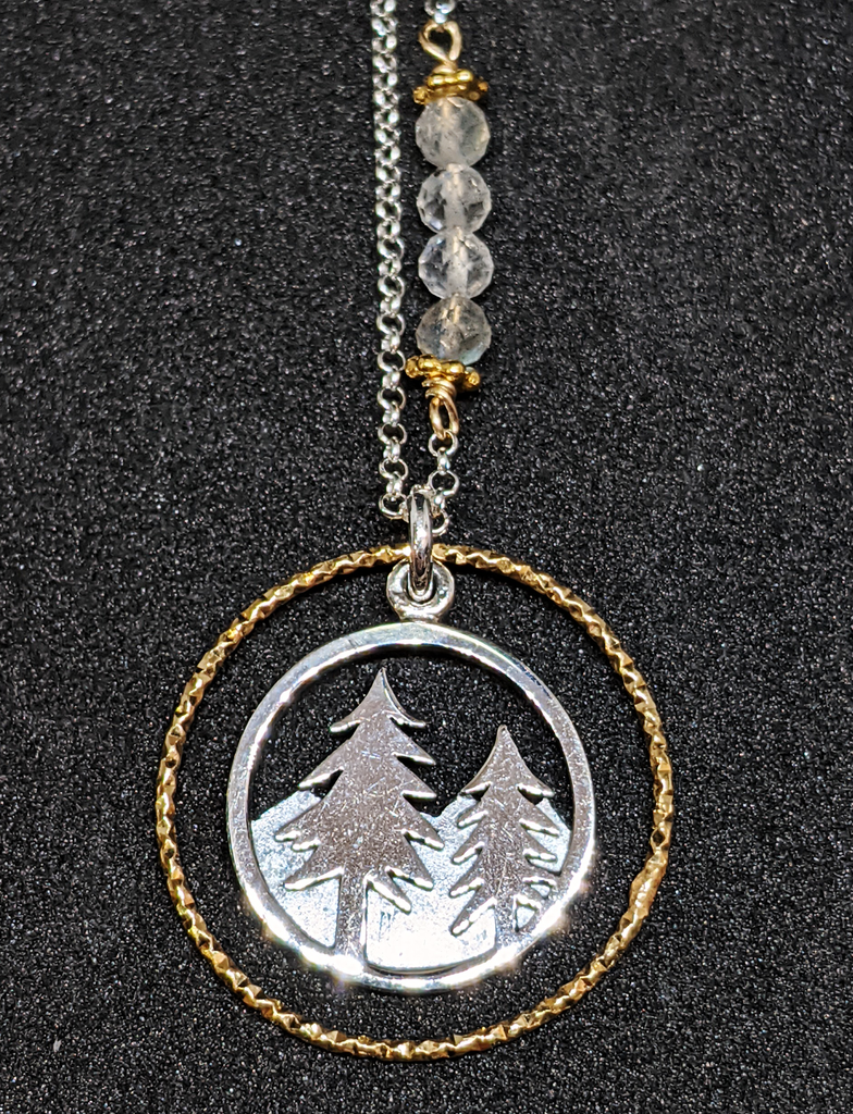 Silver chain with four coloured beads in middle of chain attached with gold chain links that look like flowers. Pendent is a gold ring that has triangle ridges. Silver ring in the middle that has pine trees in the front and mountains in the back.