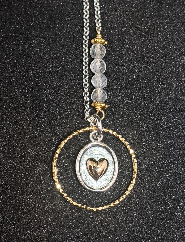 Silver chain with 5 coloured beads in middle of chain attached with gold chain links that look like flowers.  Pendent is a gold ring that has triangle ridges. Inside of gold rind is an oval with a silver outline and grey background. There is a gold heart in the center. Necklace is on a black background.